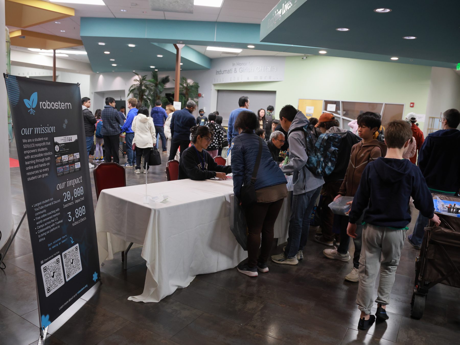 Families and students queue at the RoboSTEM check-in table beside our banner in the lobby of the India Community Center