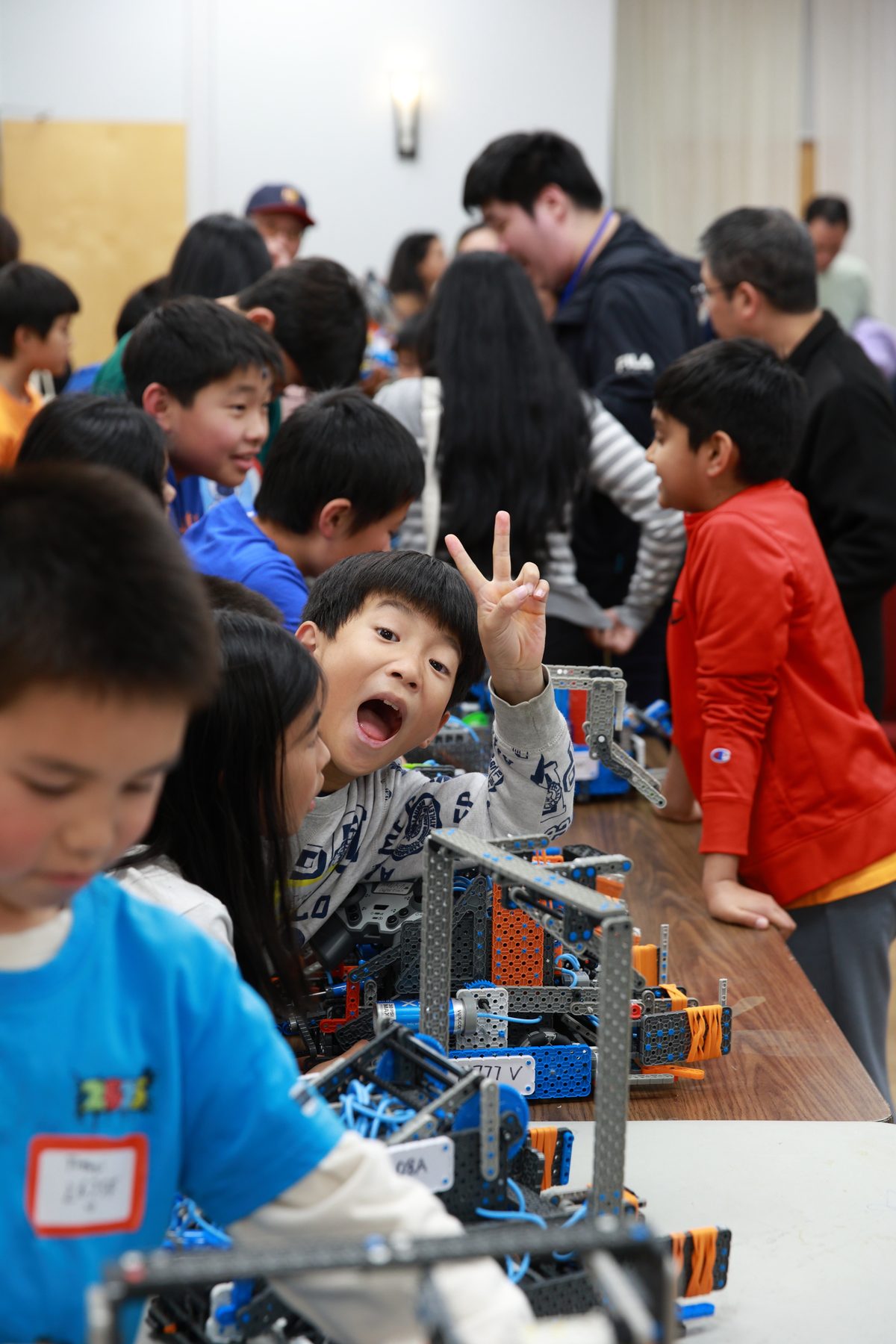 A student flashes a peace sign from the pit tables, robots lined up in front